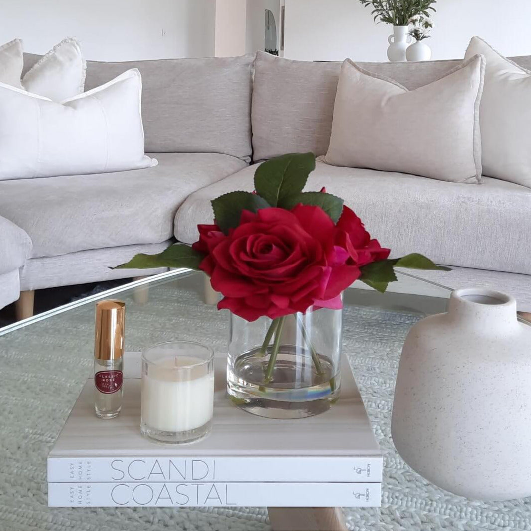 3 artificial red roses arranged in a glass vase paired with a classic rose fragrance spray