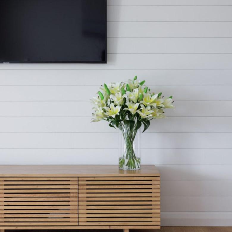 Artificial silk white lily flower arrangement in high quality glass vase positioned on tv unit