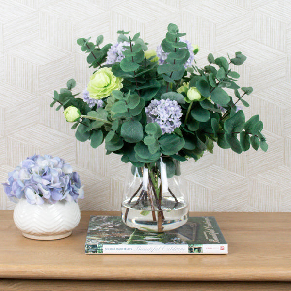 Artificial flowers and eucalyptus leaves in glass vase