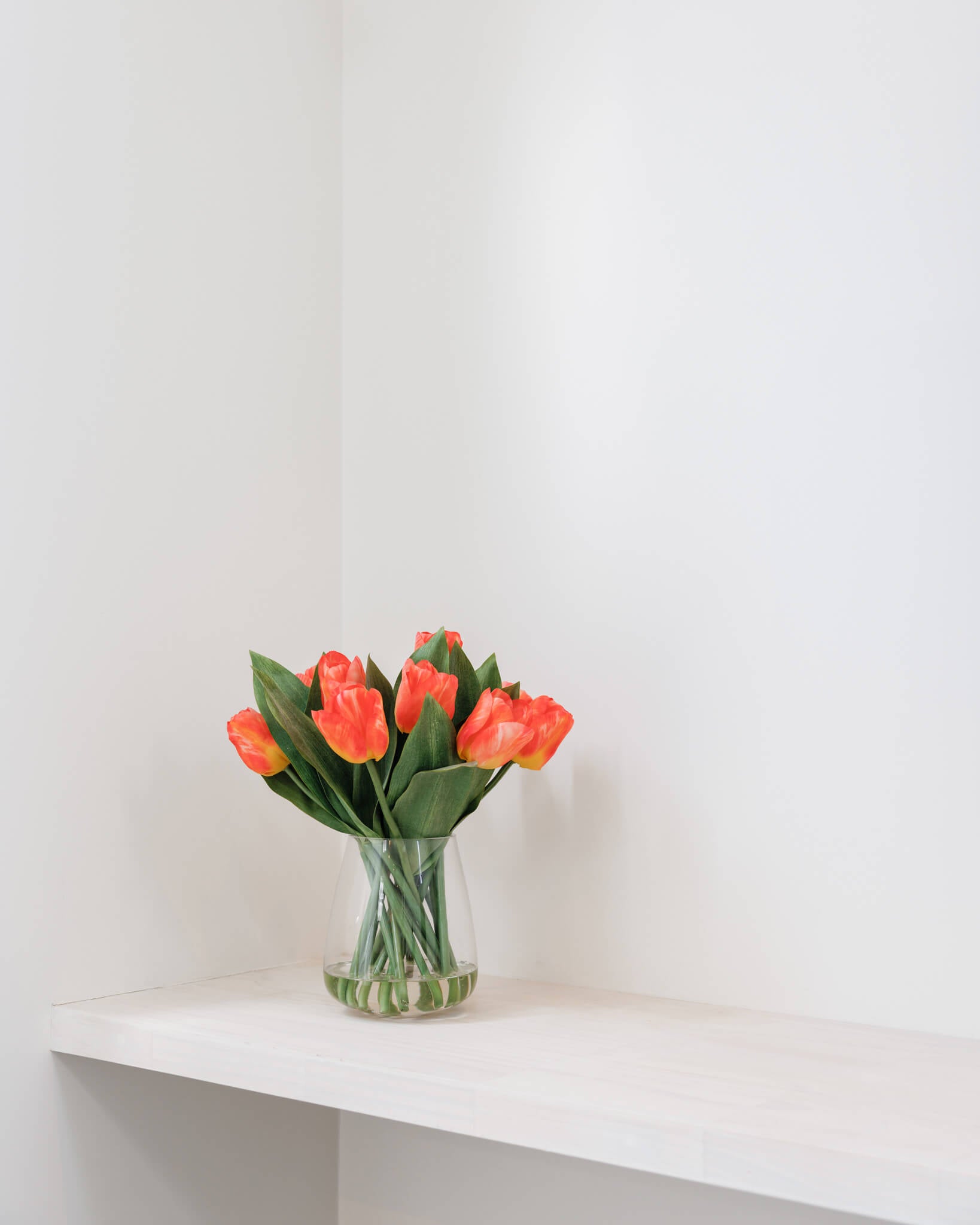 Faux orange tulips in glass vase adding colour to a dull space at home