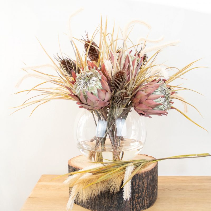 Fake protea flower arrangement in glass vase