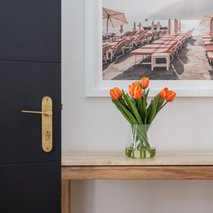 Fake orange tulip bouquet set in glass vase in the entryway to a home