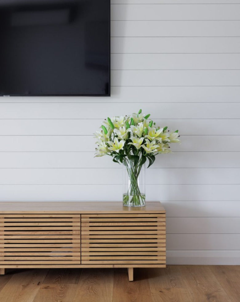 Artificial silk white lily flower arrangement in high quality glass vase positioned on tv unit
